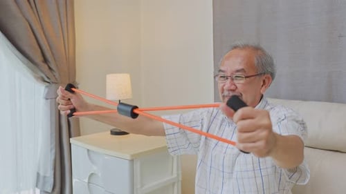 Close up of Happy Asian Disabled senior elderly man sitting alone on sofa doing physiotherapy.