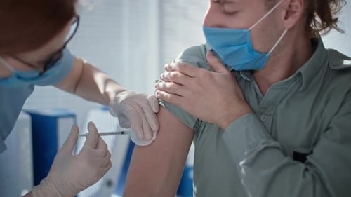 Una doctora vacuna a un joven enmascarado con jeringa y aguja durante la pandemia de coronavirus