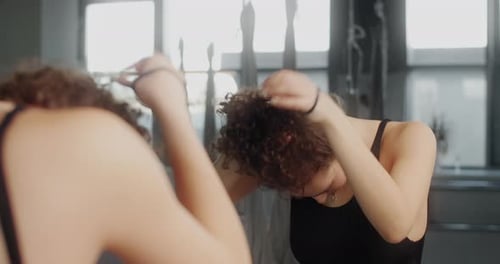 Attractive Young Cubinian Woman Makes a Bun From Her Long Curly Hair Infront of Mirror Wall of Dance