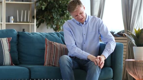 Homem de meia idade com dor no joelho sentado no sofá