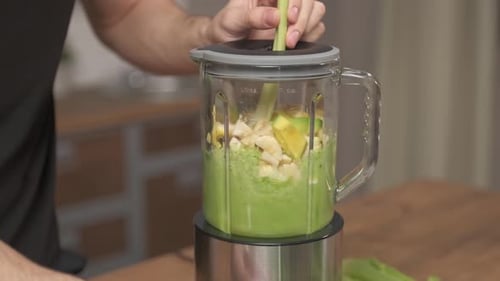 Making green juice at home: Male hands mixing vegetable smoothie in glass blender at home kitchen.