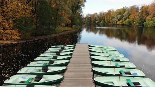 Boats Moored Along Wooden Pier on River in Autumn Park