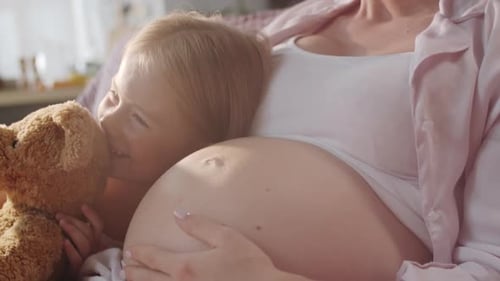 Garota alegre segurando um brinquedo e se relacionando com uma mãe grávida amorosa