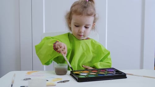 A Young Artist of Two or Three Years Draws Color Circles in Watercolor on White Paper.