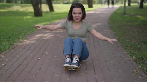 Foto de Dolly de una persona pequeña y alegre sentada en patineta en el parque de verano en el callejón