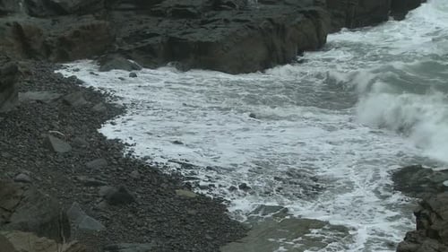 Waves breaking into foam on a rocky beach in Maine.