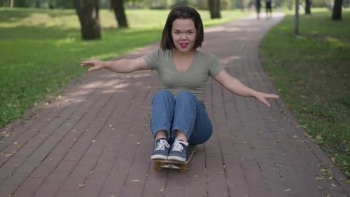 Foto de Dolly de una persona pequeña y alegre sentada en patineta en el parque de verano en el callejón